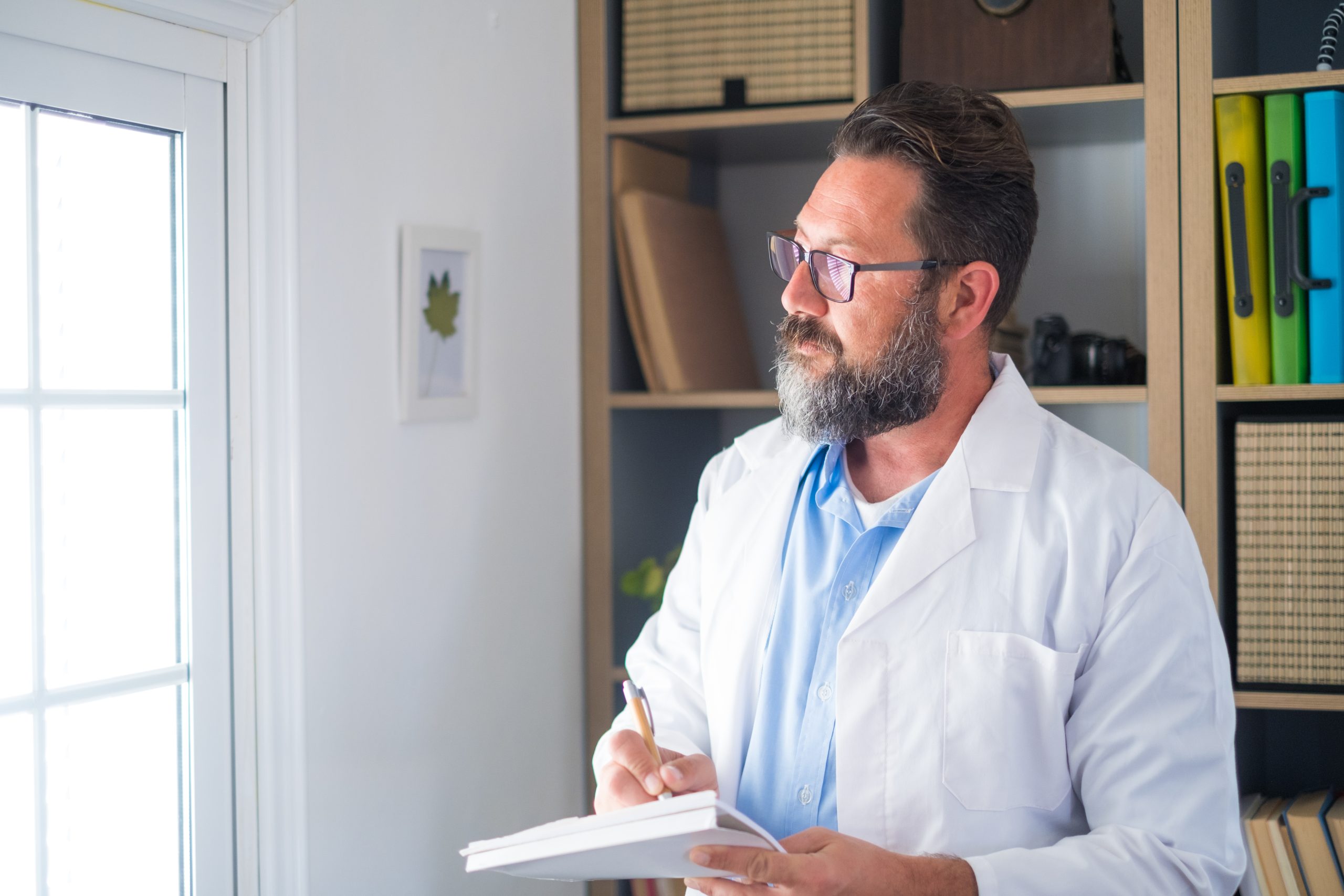 Pensive young male caucasian doctor in white medical uniform look in window distance thinking or pondering, serious man GP plan future career or success in medicine, visualize at workplace writing